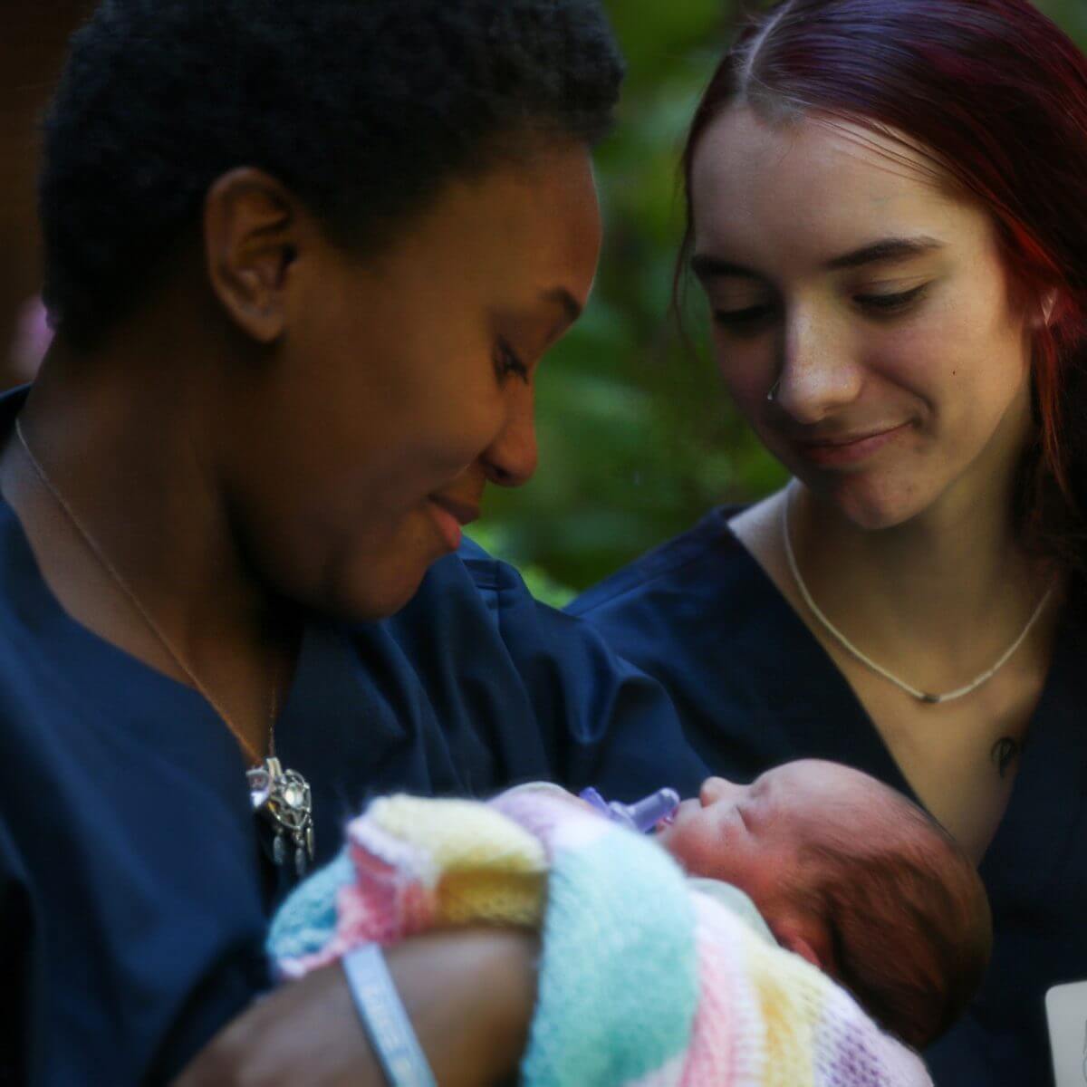 A Volunteer Center caregiver in scrubs smiling as she holds a sleeping newborn